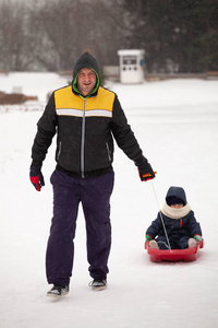 父亲把孩子拉上雪橇。父子俩在冬天拉雪橇。