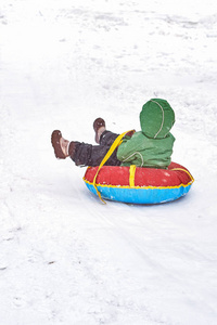 小男孩在冬天拉雪橇。孩子坐着管子滑下山来
