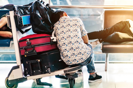 在机场候机楼等待登机时，疲惫的乘客在手推车上打盹。