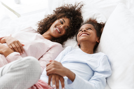 Image of cheerful african american woman and her daughter lying 