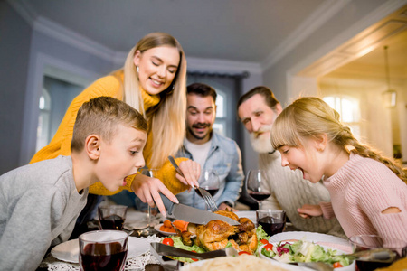 感恩节庆祝传统家庭晚餐概念。有趣的照片，一家人坐在桌旁，母亲正在切火鸡，两个小朋友兴奋地张嘴看着食物
