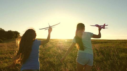 梦想飞翔。快乐童年观。两个女孩在日落时玩玩具飞机。孩子们在太阳的背景下，手里拿着一架飞机。孩子们在飞机上玩耍的剪影