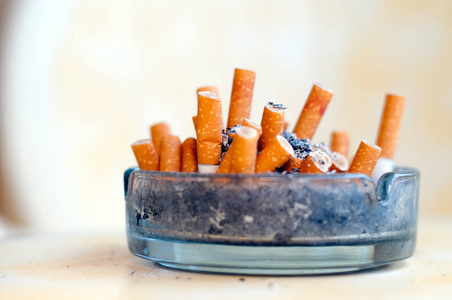 桌子上的香烟桌子上的玻璃烟灰缸里有许多烟头和烟灰照片