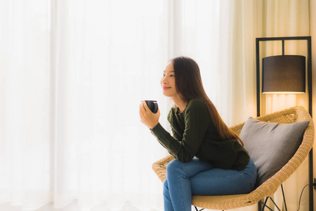 美丽的亚洲年轻女子捧着咖啡杯坐着