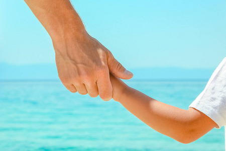 快乐的爸爸在大自然的希腊海边牵着孩子的手