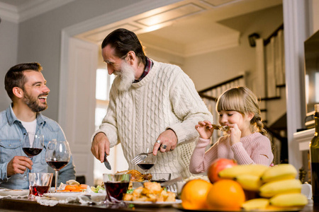 快乐的老爷爷和儿子孙女在节日餐桌上切火鸡