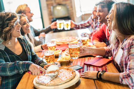年轻的朋友在家里吃披萨在冬天的团聚友谊的概念与快乐的人享受时间在一起，并有乐趣喝啤酒品脱舒适的晚餐地点集中在啤酒杯
