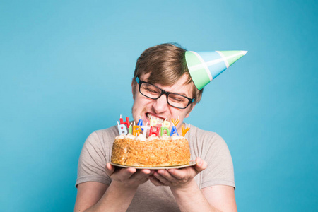 一个滑稽的男人戴着纸制的祝贺帽，试图咬下一个蛋糕，蓝色背景上放着生日快乐的蜡烛。