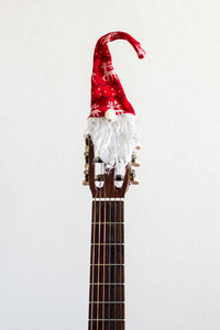 带红色圣诞帽的原声吉他。白色背景上的圣诞歌曲音乐概念