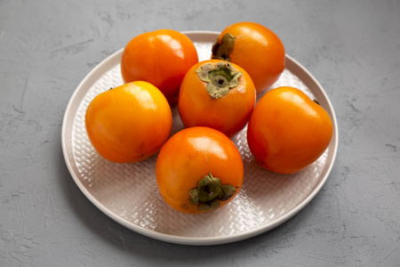 Raw Ripe Orange Persimmons on a plate over gray background, low 