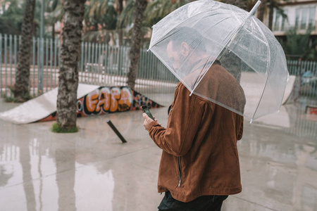 男子在雨中打着透明伞看着手机图片