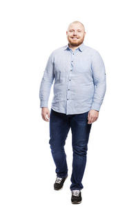 Smiling redhead man with a beard in jeans and a blue shirt. Full