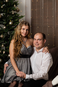美丽快乐的男人和女人在沙发上的新年树前。新年快乐。