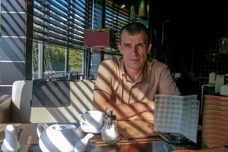 Young man drinking a coffee at the cafe. The shadow of the mesh 