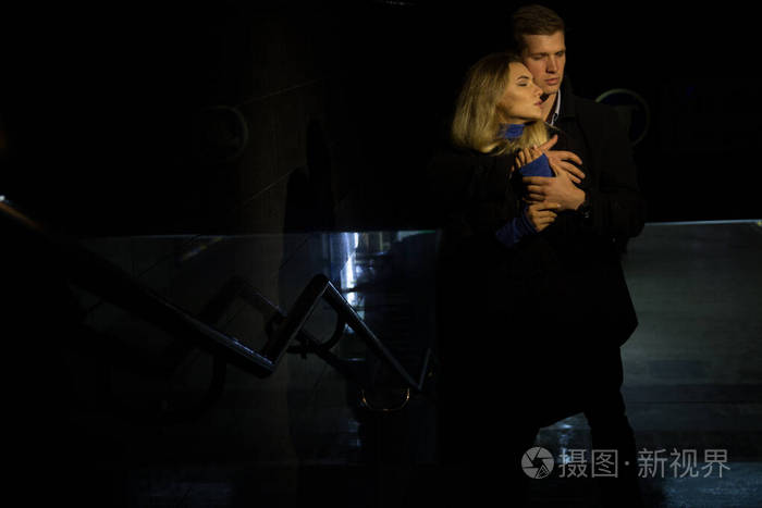 一对相爱的情侣在黑暗的背景下拥抱夜晚下雨城市里的建筑物一个公园