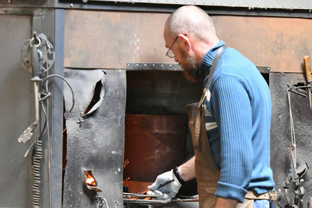 铁匠在炉子里加热铁。年轻的传统铁匠明火作业铁匠在铁厂里用火花焰火生火在车间里锻造热铁