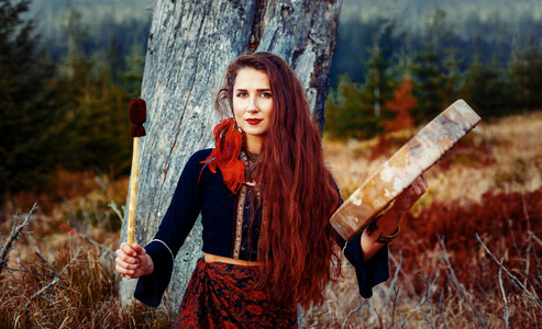 美丽的萨满教女孩在大自然中的萨满框架鼓.照片