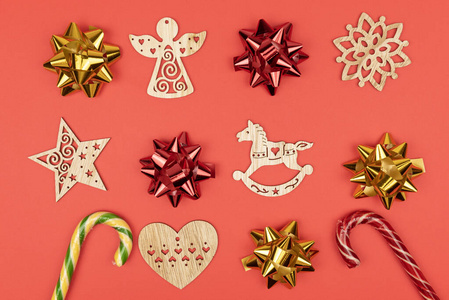 节日装饰品。红色和金色蝴蝶结组成的构图，木制圣诞树玩具，红色背景上的糖果手杖。俯视图，特写
