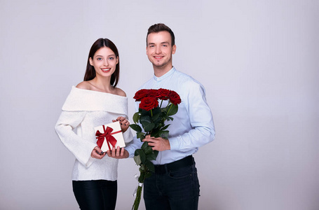 一对恩爱夫妻拿着礼物和红玫瑰摆姿势，微笑着。