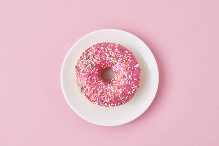 donat在粉色背景上用白色盘子装饰花洒和糖霜。创意和极简的食物概念，俯视平面