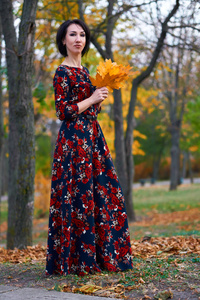美丽优雅的女子站在秋天的城市公园与一束黄叶合影
