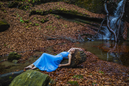 秋日瀑布边，一位身穿蓝色连衣裙的美丽女子