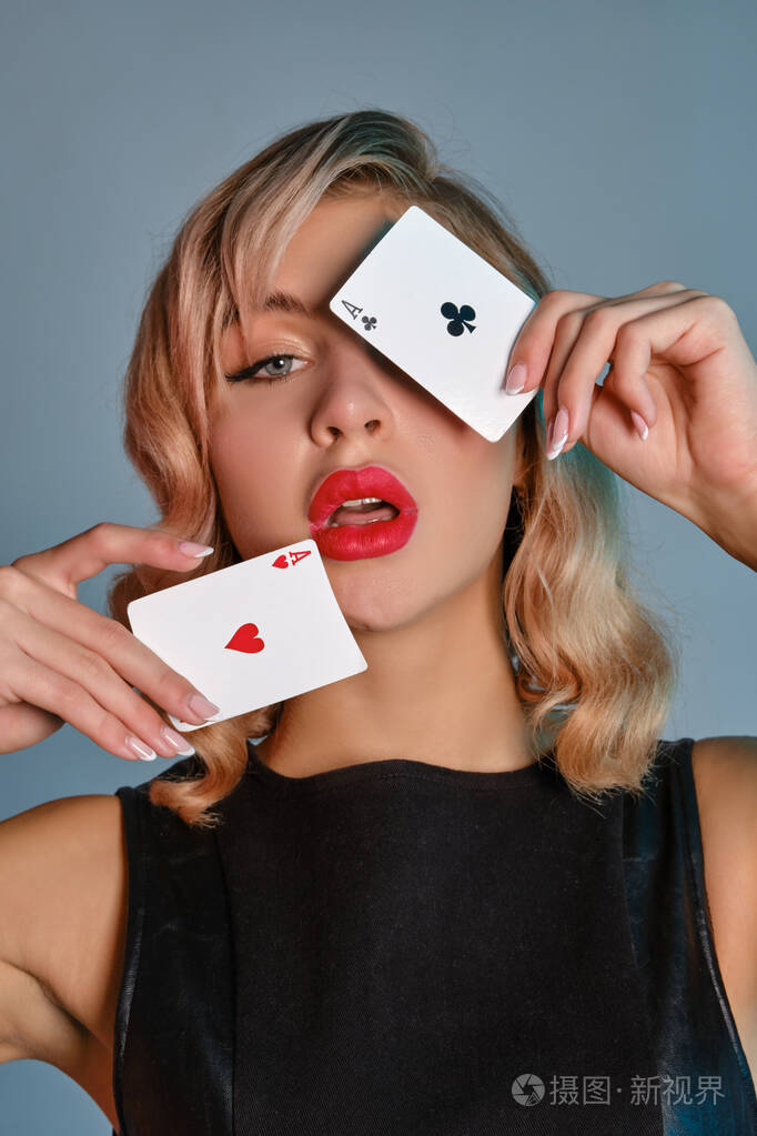 身穿黑色皮衣的金发女孩在灰色背景下摆出两张扑克牌.