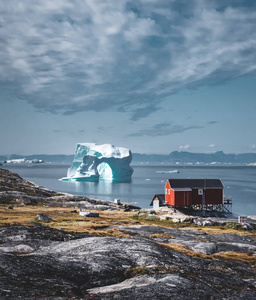 南极格陵兰水域中的一座拱形冰山，以北极半岛的山脉为背景。晴天蓝天白云，五彩缤纷的小房子。