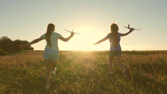快乐童年观。梦想飞翔。两个女孩在日落时玩玩具飞机。孩子们在太阳的背景下，手里拿着一架飞机。孩子们在飞机上玩耍的剪影