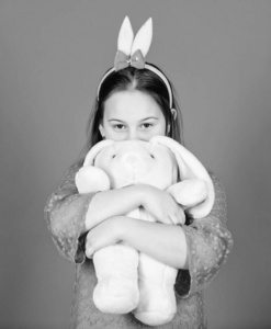 快乐的童年。带着复活节的精神。兔子耳朵配件。可爱顽皮的小兔子抱着柔软的玩具。祝福复活节。蓝色背景上有可爱玩具的兔女郎。小孩笑着玩