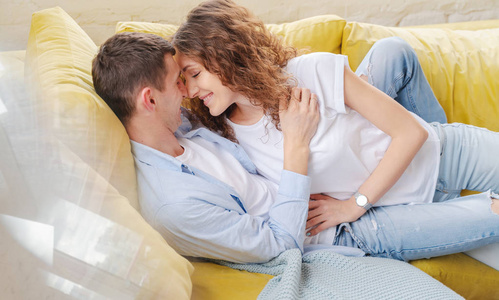 Young happy couple lying and hugging on the yellow couch in the 