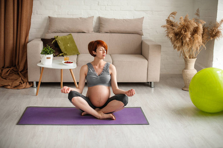 一位年轻漂亮的孕妇坐在家里的健身球旁。