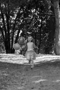 小可爱的女孩拿着一堆气球在公园里跑。她笑得很挑逗。快乐童年的概念。