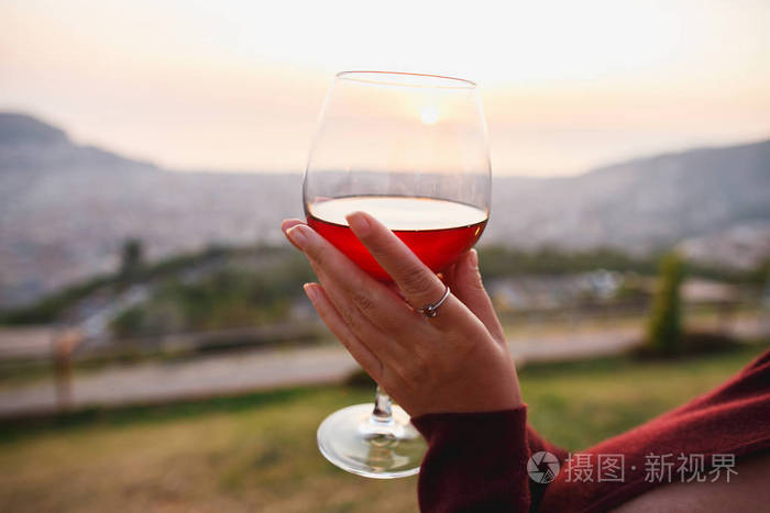 夕阳山上的女人拿着红葡萄酒近距离手持优雅的玻璃杯酒体呈深红色