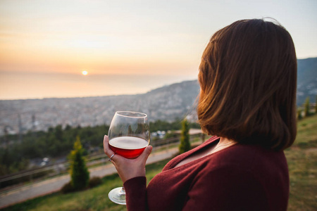 女人在夕阳山上喝红酒,特写手持酒杯.