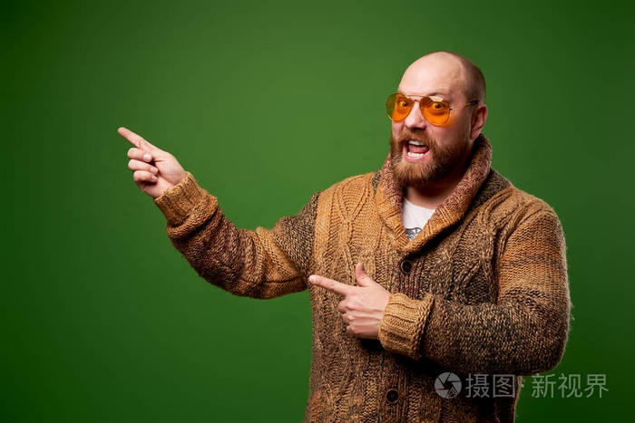 穿着毛衣的快乐男人在绿色的背景下用手指着空旷的地方