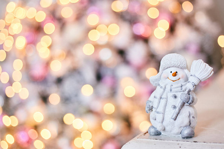 Snowman toy on the background of a Christmas tree and garlands. 