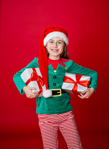 圣诞快乐，快乐迷人的女孩与礼物，在明亮的红色背景下，穿着圣诞老人小精灵的服装。