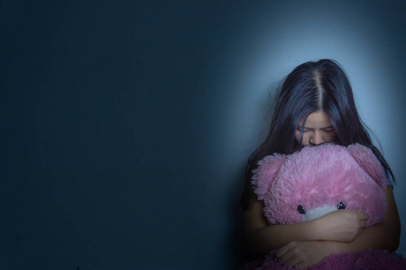 膝盖黑一个悲伤的女人抱着她的膝盖哭着坐在黑暗中的泰迪熊照片