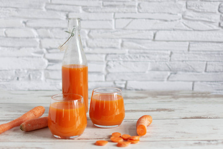 把胡萝卜汁放在玻璃杯里，新鲜的胡萝卜放在桌子上。在木制桌子背景上的玻璃杯里放着健康的减肥饮料。