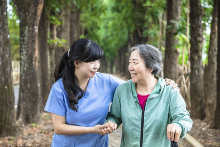 微笑的护士帮助老年妇女在公园里散步