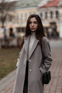 秋日，一个棕色头发的年轻女子穿着时髦的外套，穿着温暖的复古高尔夫，拎着包在城市里摆姿势。时尚女孩站在街上。春秋风格。