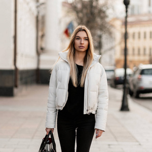 在一个温暖的秋日里，一位身着黑白时尚服装拎着一个时髦皮包的时髦金发女郎在街上散步。欧洲女时装模特喜欢在城市里散步。