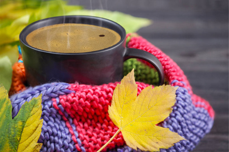 Black coffee in a black mug wrapped in a warm, colored, knitted 