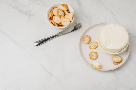 奶酪和饼干放在一个白色的碗里，在白色的大理石上放一把刀