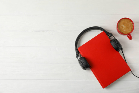 Red book, headphones and coffee cup on wooden background, space 