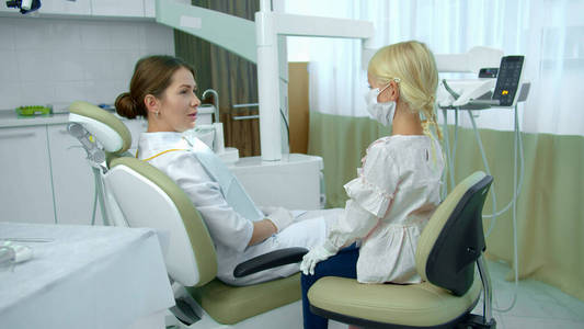 牙医坐在病人椅上和女孩交谈