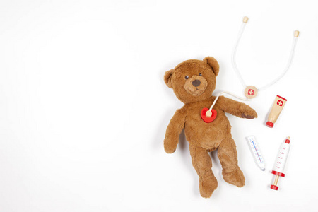 白色背景上有玩具听诊器和玩具医疗工具的泰迪熊。俯视图。复制文本空间