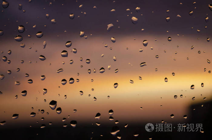 窗外的雨落在夕阳的背景下下雨时雨滴落在玻璃上明亮的水滴质地