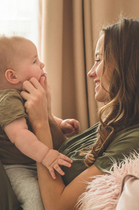 Home portrait of a baby boy with mother on the bed. Mom holding 